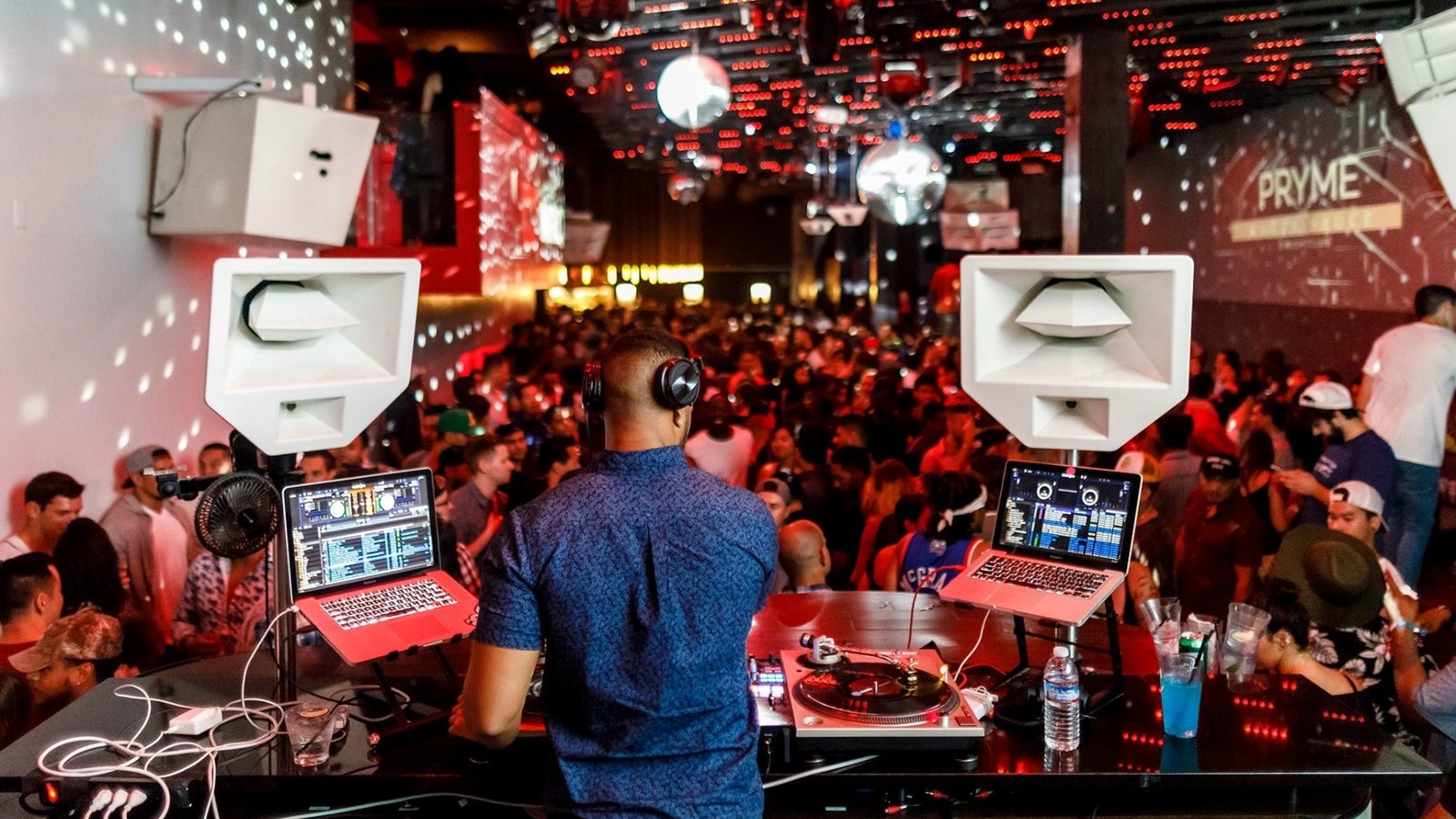 View from behind the DJ booth of a packed club floor with PRYME on the screens